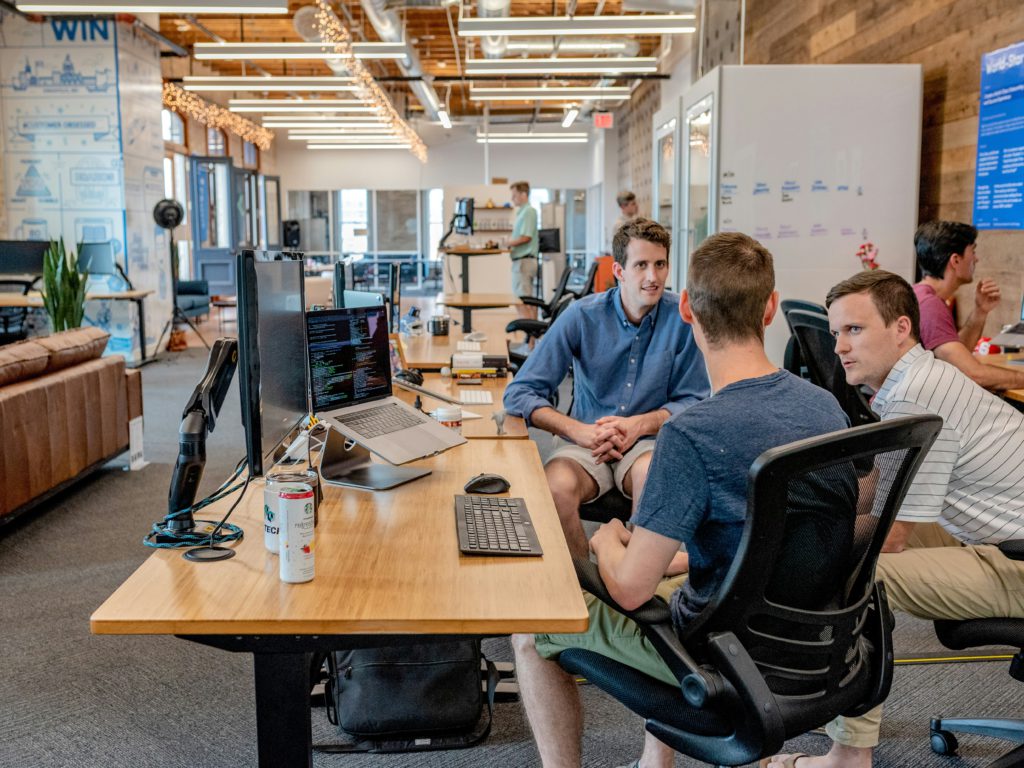 three male colleagues at work in front of computers employees working collaborating business meeting